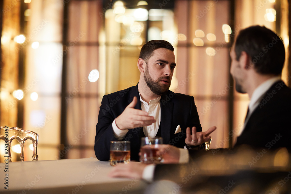 Portrait of handsome businessman discussing work with partner sitting at table in luxury restaurant, copy space