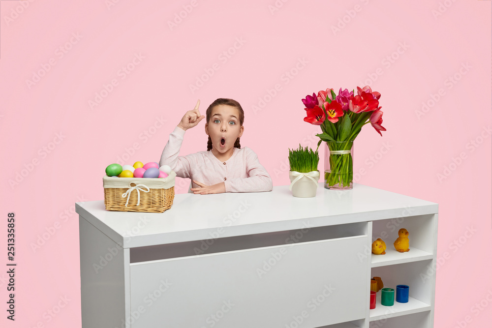 Girl with finger up at table with Easter eggs Girl with finger up at table with Easter eggs