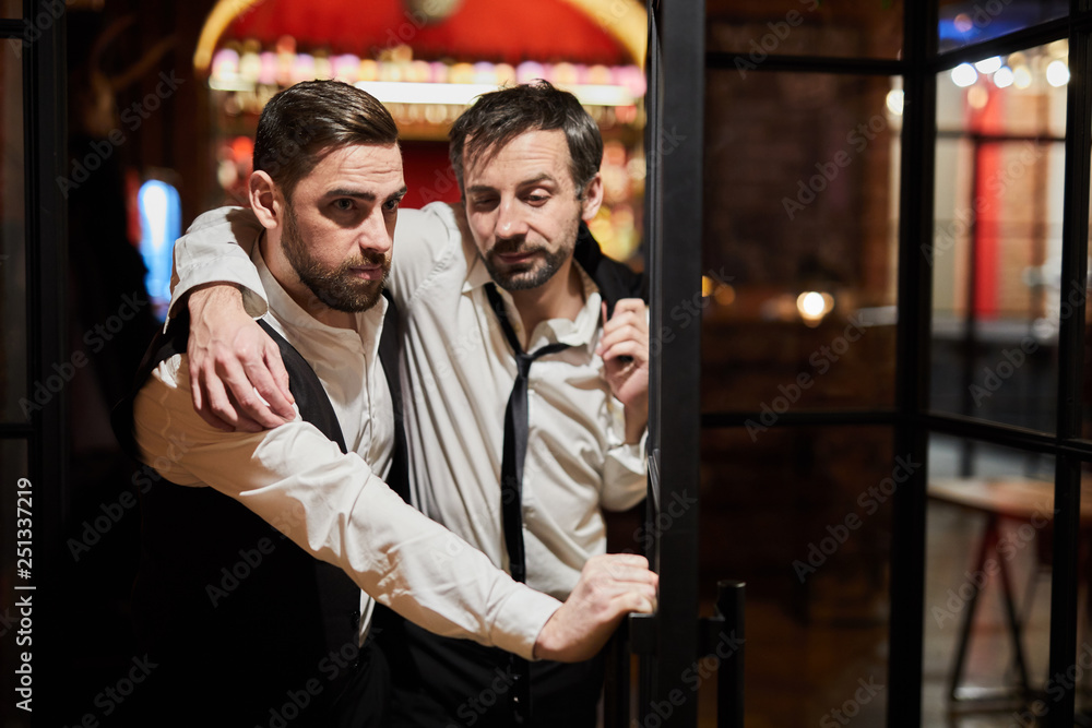 Waist up portrait of waiter carrying drunk man out of bar, copy space