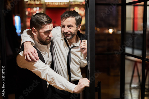Waist up portrait of waiter carrying drunk man out of bar at night, copy space