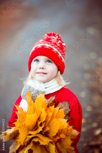 little girl 4 years old in a red hat and coat walking in autumn park in October, during the golden autumn with a bouquet of yellow maple leaves smiling © Евгения Янцева