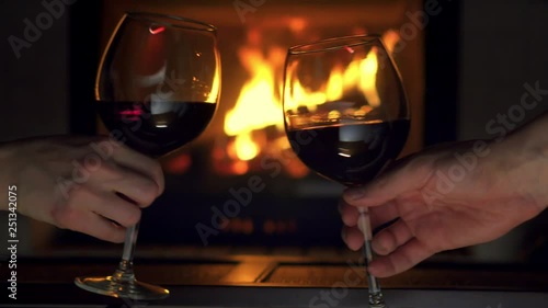 Close-up man and woman hands toasting clink glasses with red wine fireplace in background. Winter evening romantic atmosphere couple celebrating holiday cheers goblet with beverage