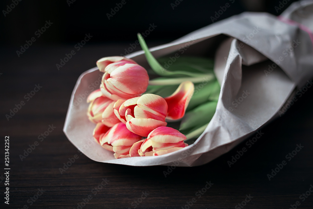 Five roses in a peach-colored kraft paper on a dark wooden background, natural light, horizontal arrangement