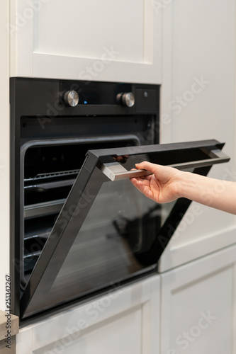 Woman hand opening black built-in oven in white kitchen cabinet