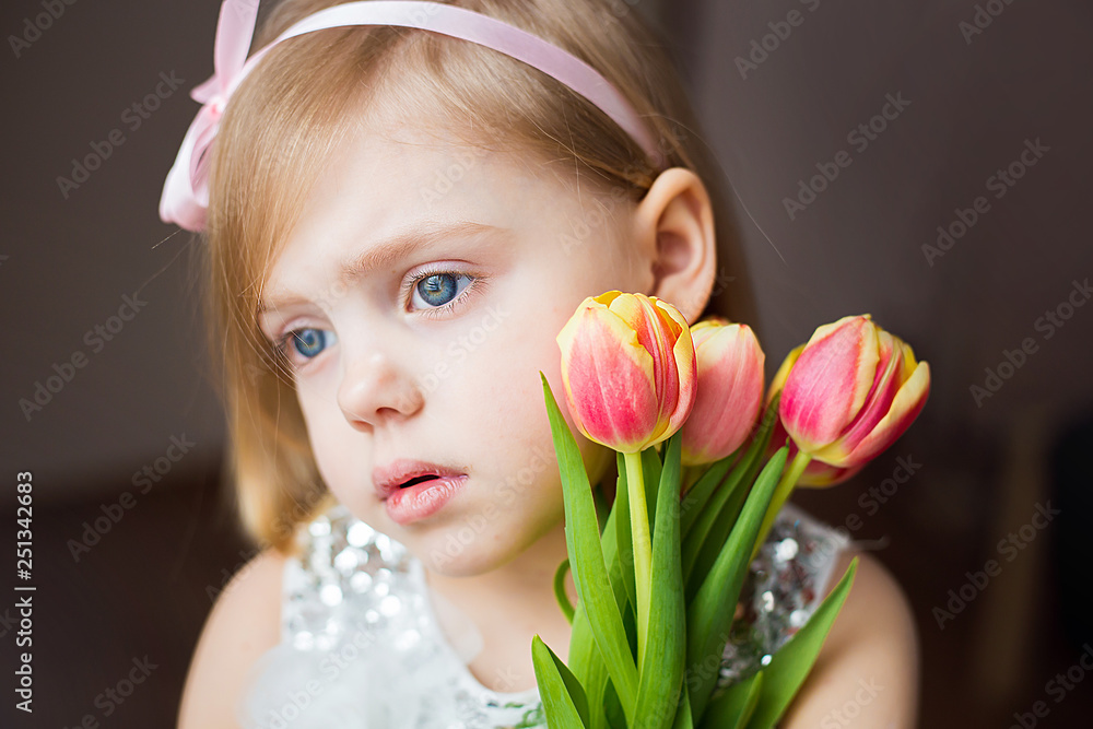 cute little blonde girl of three years with peach tulips close-up, sad, side view, horizontal photo,