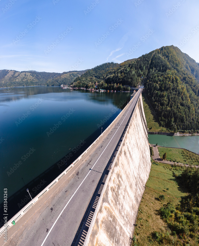 Aerial scenic view of a dam constructed on a beautiful valley in mountains. water storage reservoir. road with beautiful views for travel and holidays. lake Lzvorul Muntelui, Romania, vertical photo
