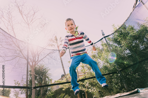 5 year old boy jumping on a trampoline exercising in the backyard of his house, enjoying the spring with gesture of happiness and lifestyle.