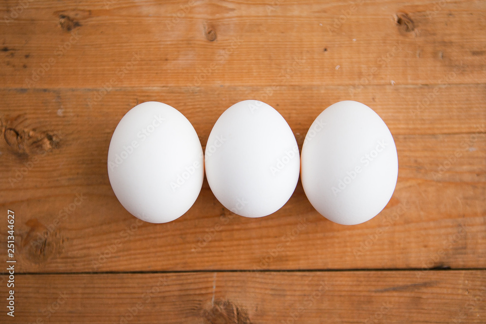 Three white eggs in a raw on a wood ground Three white eggs in a raw on a wood ground