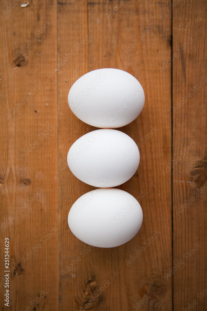 Three white eggs in a raw on a wood ground Three white eggs in a raw on a wood ground