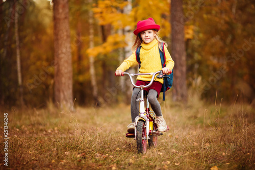 Fototapeta Naklejka Na Ścianę i Meble -  cheerful blonde babe 6 years old in a red hat yellow sweater in autumn riding a bike in the park or in the woods