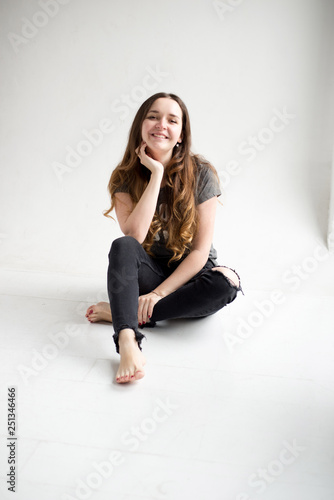 Portrait of a smiling young girl sitting on white background in nice stylish cloth. young pretty woman isolated on white. girl in torn jeans and t-shirt