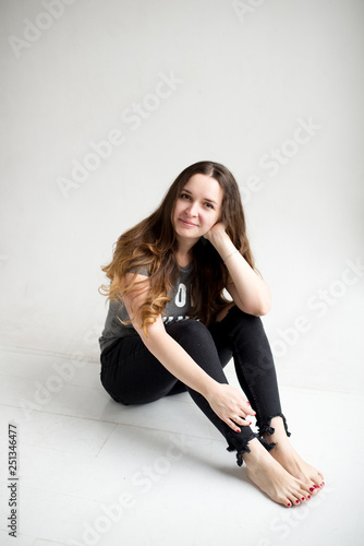 Portrait of a smiling young girl sitting on white background in nice stylish cloth. young pretty woman isolated on white. girl in torn jeans and t-shirt