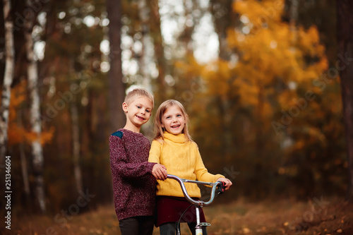 happy child, baby girl little 6 years old in a red hat on a bicycle rides, her brother, a boy 7 years old run along the park in the golden autumn