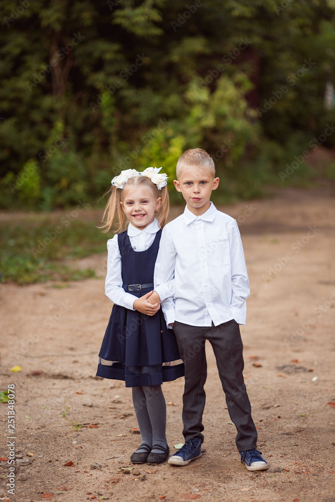 Obraz premium beautiful cheerful children, schoolchildren of 7 years, ready for the beginning of the school year, in school uniform stand on the street in an embrace and smile
