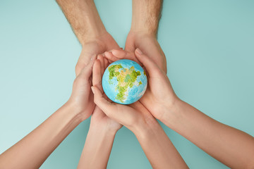 top view of man and woman holding planet model on turquoise background, earth day concept