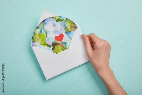top view of woman holding envelope with planet picture on turquoise background, earth day concept