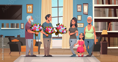 happy multi generation family congratulating women with international 8 march day concept men giving flowers living room interior full length horizontal flat