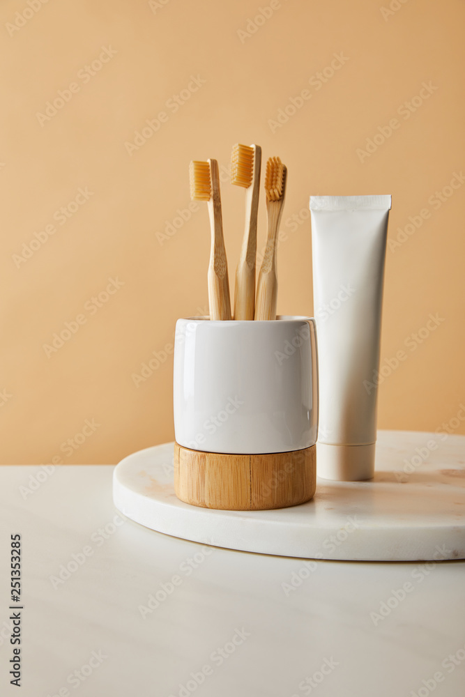 Naklejka premium toothpaste in tube and holder with bamboo toothbrushes on white marble surface and beige background