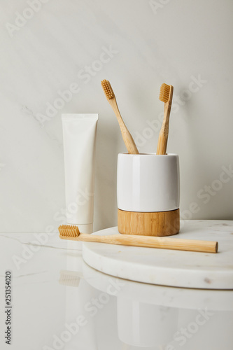 bamboo toothbrushes, holder and toothpaste in tube on white marble background