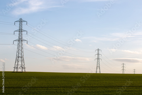 Electricity pylons in landscape with green field and blue sky
