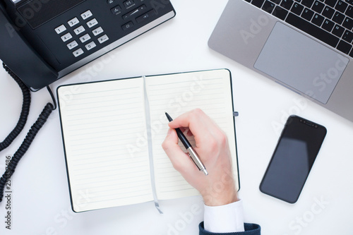 Male hand, laptop, IP phone, mobile phone and notebook on the white background. Top view. Ip telephony and video meetings for business concept. 