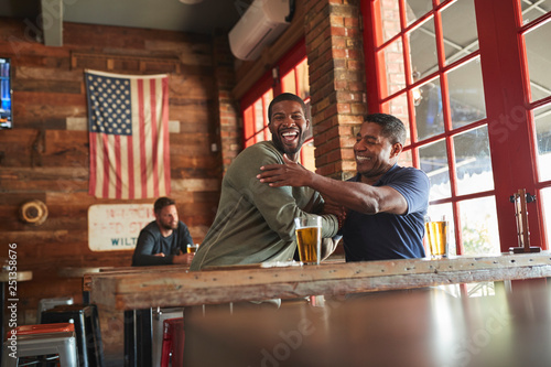 Two Male Friends Greeting One Another In Sports Bar Enjoying Drink Together