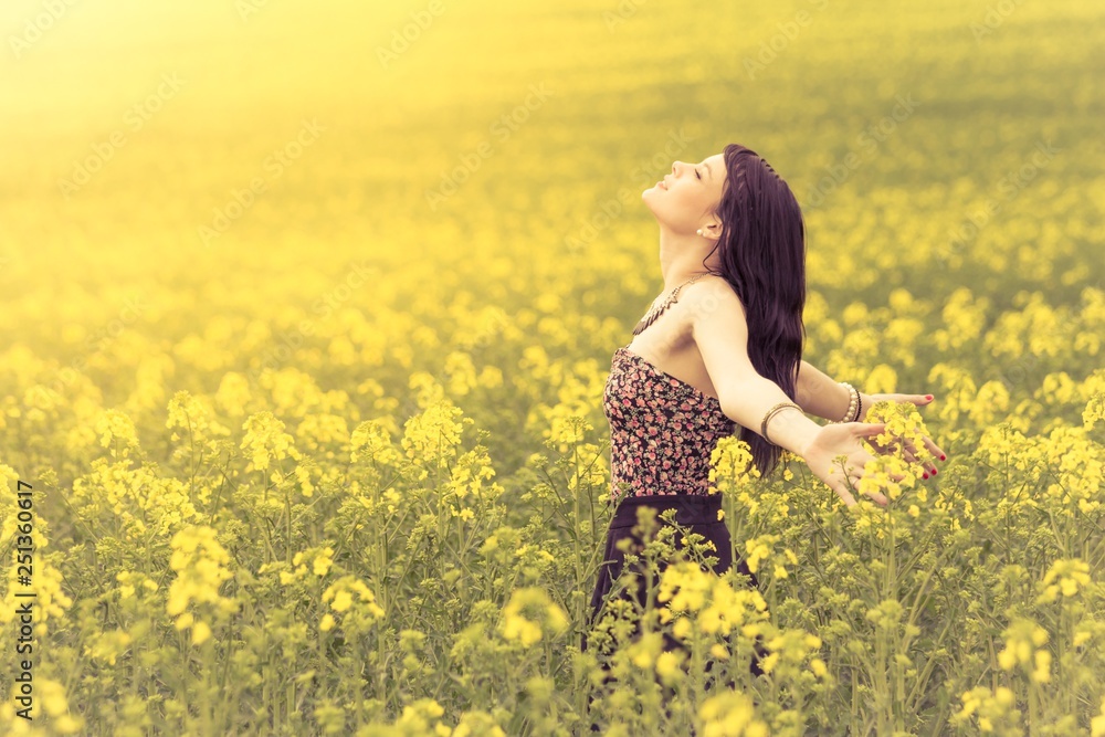 Fototapeta premium Free beautiful woman in happy summer love of youth wellbeing. Attractive young beauty girl enjoying the warm sunny sun in nature rapeseed field takes time feeling sustainability and contemplation