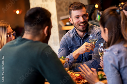 Group of young friends having fun in restaurant  talking and laughing while toasting with glass of wine.