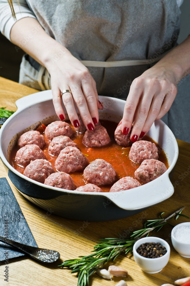 The chef prepares Italian meatballs from raw minced meat, puts in a baking dish with tomato sauce. Black background, top view, kitchen