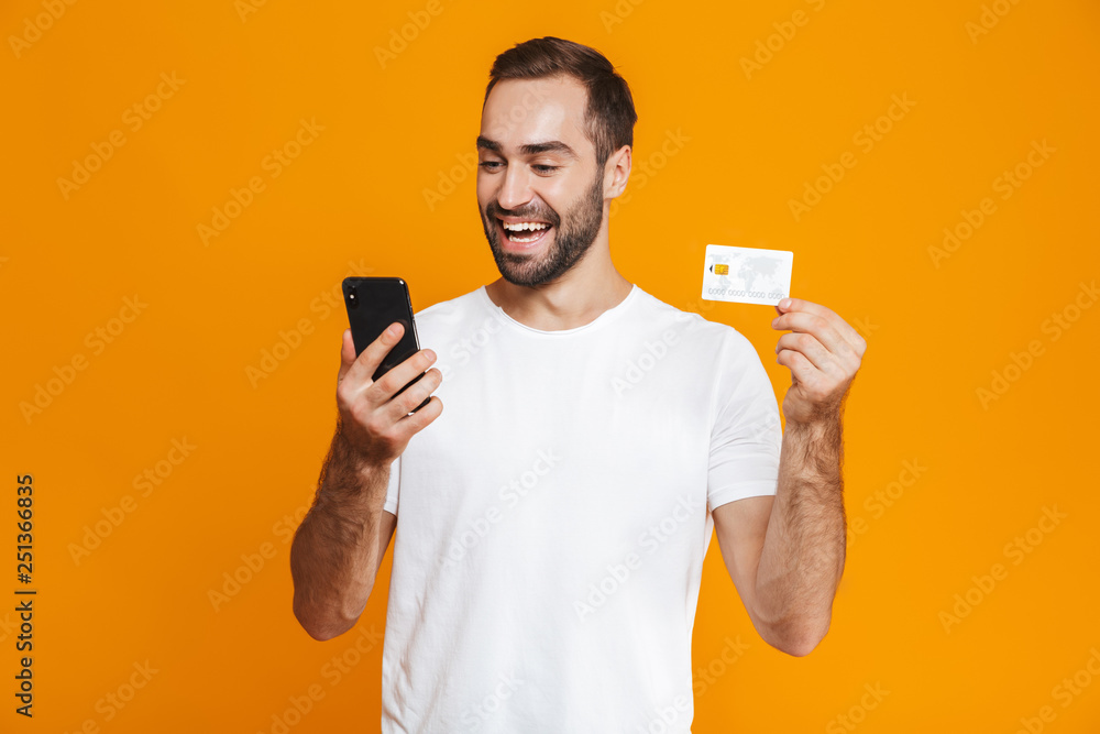Photo of caucasian man 30s in casual wear holding smartphone and credit card, isolated over yellow background Photo of caucasian man 30s in casual wear holding smartphone and credit card, isolated over yellow background
