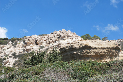 Large white stones among green plants against the blue sky, Cape Fourny, Rhodes Island, Greece