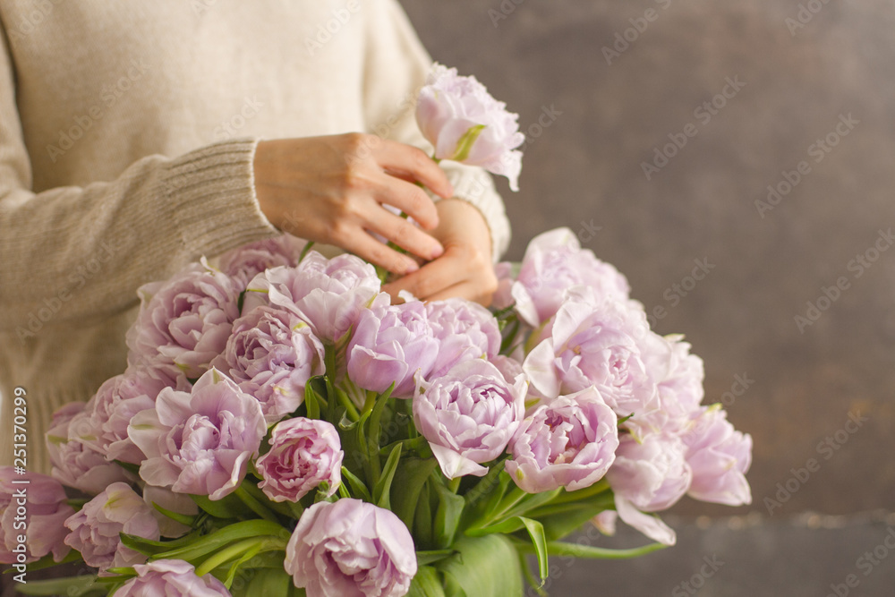Florist at work: pretty young woman making a big bouquet of double violet tulip flowers on a dark rustik background Florist at work: pretty young woman making a big bouquet of double violet tulip flowers on a dark rustik background