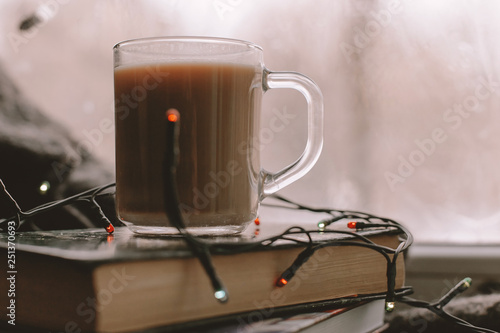 Coffee in transparent Cup is worth on books. Coffee, books and a blanket on the windowsill. Heart on the frozen window. A cozy winter day with coffee and books.