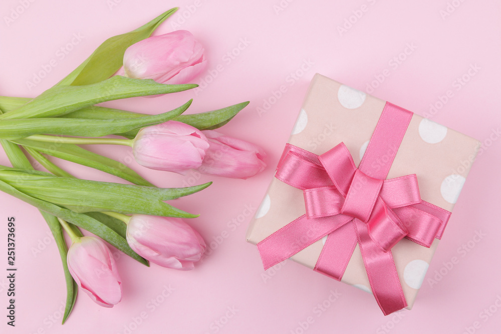 A bouquet of beautiful pink tulips flowers and a gift box on a trendy pink background. Spring. holidays. top view.