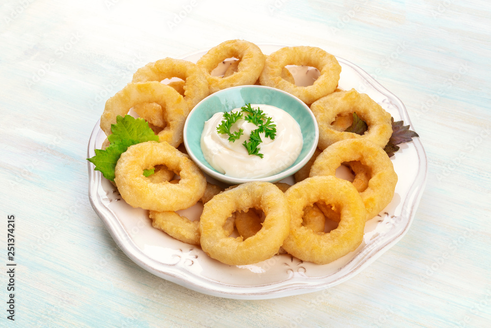 A closeup photo of squid rings with mayonnaise and green leaves A closeup photo of squid rings with mayonnaise and green leaves