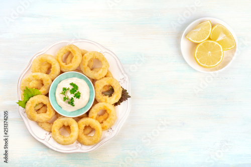 A photo of squid rings with mayo and lemon wedges, shot from the top, forming a frame for copy space