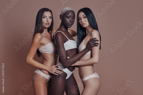 Effortless beauty. Three attractive mixed race women looking at camera while standing against brown background