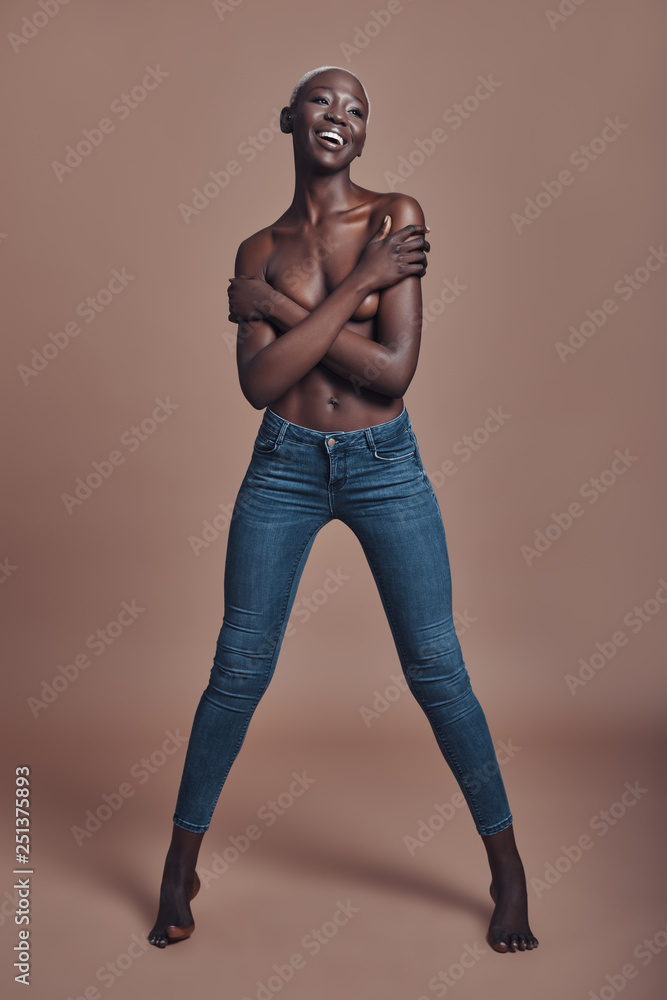 Sensual woman. Full length of attractive young African woman looking at camera and covering breast with hands while standing against brown background Sensual woman. Full length of attractive young African woman looking at camera and covering breast with hands while standing against brown background