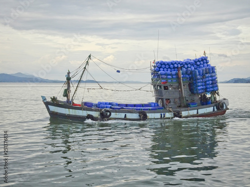 Cargo boat floats on the sea laden with barrels of water, Thailand.