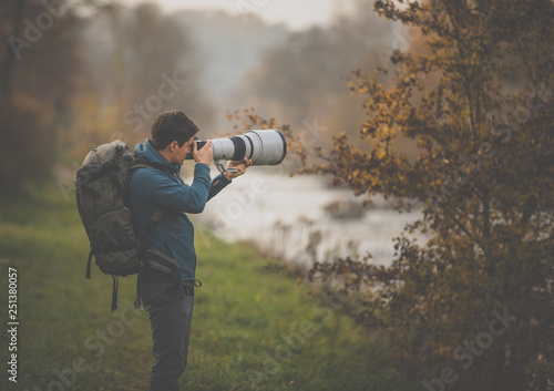 Young man devoting time to his favorite hobby - photography - taking photos outdoor with his digital camera/DSLR and a big telephoto lens