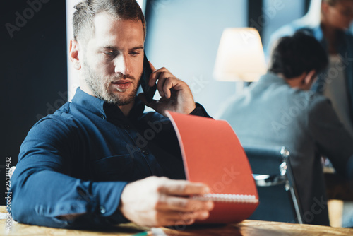 Handsome man employee sitting at the table and working with notepad and talking on mobile phone