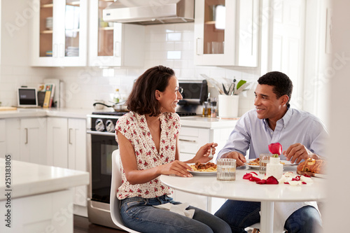 Young couple sitting at the table in their kitchen eating a romantic meal together, selective focus