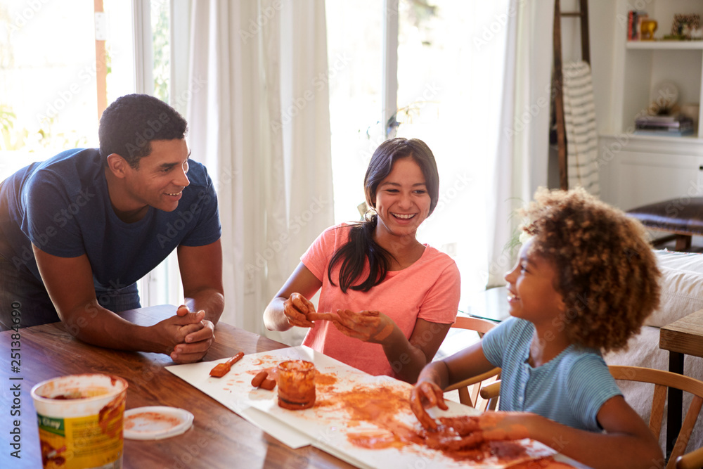 Millennial dad leaning on table watching his daughter and her girlfriend playing with modelling clay in the dining room Millennial dad leaning on table watching his daughter and her girlfriend playing with modelling clay in the dining room