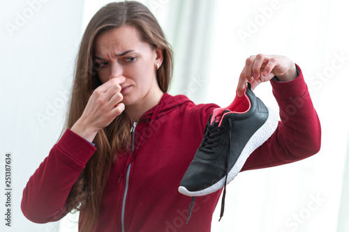 Woman is feeling unpleasant smell from sweaty running shoes after long sport training and active lifestyle. Footwear needs in cleaning and odor removal. Shoe care and shine