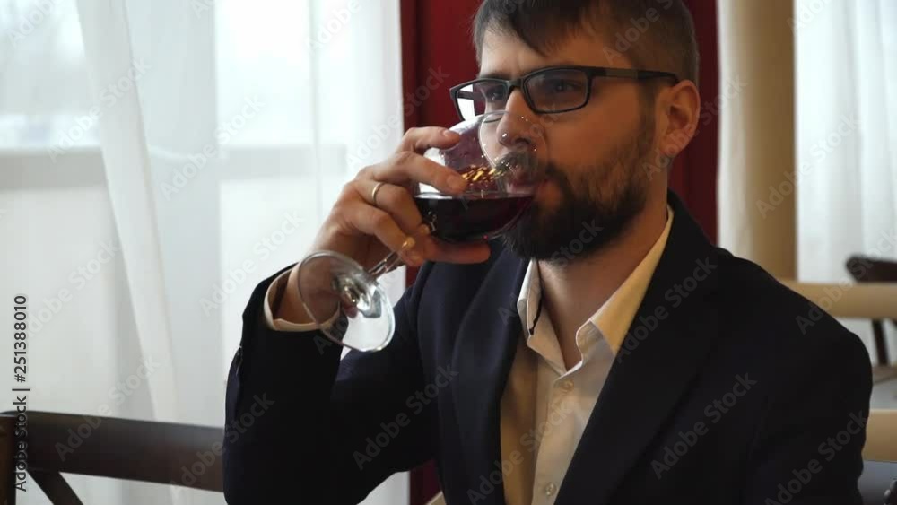 Young attractive male businessman sitting in a restaurant stirs red wine in a glass and tastes Young attractive male businessman sitting in a restaurant stirs red wine in a glass and tastes
