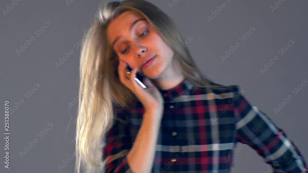 Young blonde girl in plaid dress with beautiful hair and full lips reads messages on smartphone. Woman changes in face showing her emotions. Simple beauty. Tender emotions and coquetry Young blonde girl in plaid dress with beautiful hair and full lips reads messages on smartphone. Woman changes in face showing her emotions. Simple beauty. Tender emotions and coquetry