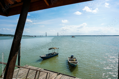 Fototapeta Naklejka Na Ścianę i Meble -  View of boat docked by the wooden jetty with johor river bridge in the background. View from a wooden jetty