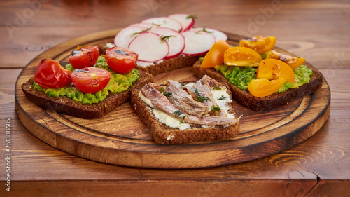 Smorrebrod - traditional Danish sandwiches. Black rye bread with fish, anchovies, avocado, tomatoes, radish on dark brown wooden background