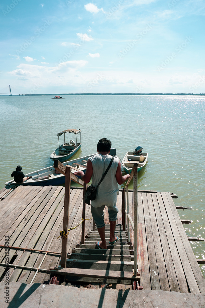 View of a man walking down the jetty stairs and a man tie a rope to secure his boat to a wooden jetty. view from a wooden jetty