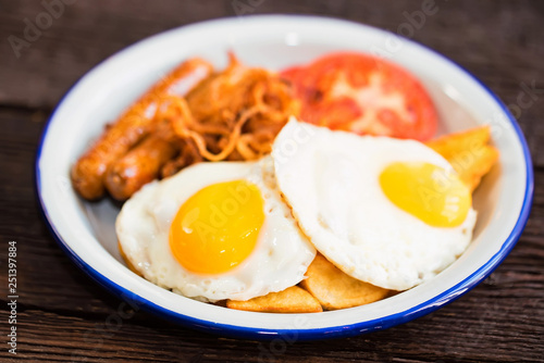 Typial breakfast with eggs, tomato, onion rings and sausage on plate